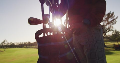 Video of midsection of african american man putting golf clubs into bag on golf field. sporty, active lifestyle and playing golf concept.