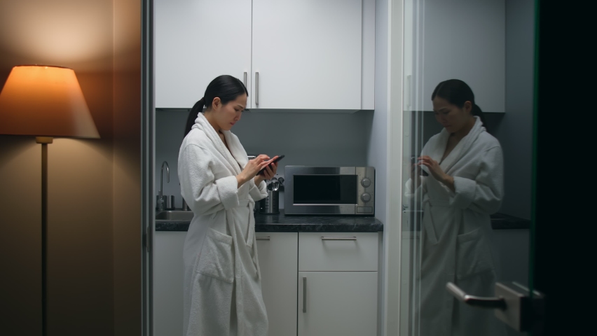 Asian woman in bathrobe receive bad email on smartphone standing in kitchen early in morning. Sad female use cellphone at home late in evening | Shutterstock HD Video #1090382275