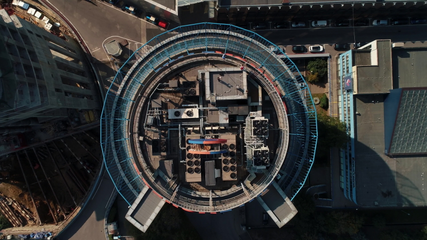 Flat rooftop of round skyscraper with different equipment and drone operators at work on sunny day upper view
