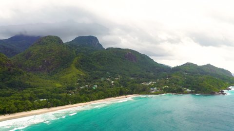 Flying above Grand Anse Beach at the Mahe Island, Seychelles, with turquoise water of the Indian Ocean, mountains and rain forests in the background. 4K UHD video.