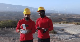 Multiracial engineer men working together on a windmill farm using digital tablet and drone - Renewable energy concept
