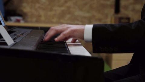 Men pianist plays gentle clerical music on a beautiful grand piano with one hand close up in slow motion. Piano keys close up in dark colors. Student trains to play the piano.