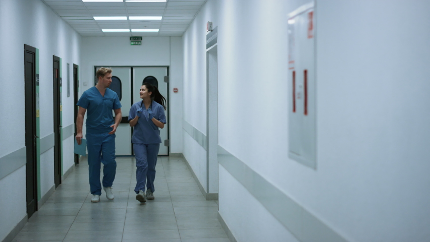 Doctors colleagues walking out doors emergency room discussing covid pandemic. Latino physician woman walking down hospital corridor with caucasian surgeon. Two medics talking about clinic work. | Shutterstock HD Video #1090387195