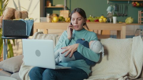 Business Mother Holding Infant and Answers the Call While Working From Home on the Couch. Woman on Maternity Leave is Working From Home. Stress Mother Concept.