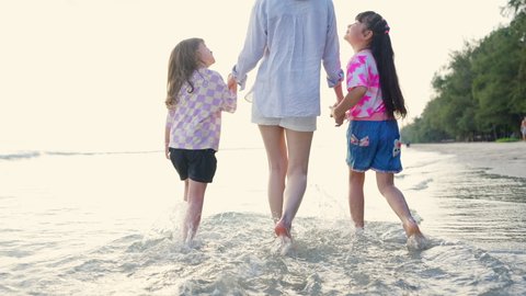 Happy Asian family on beach vacation. Mother with two little daughter walking and playing together on the beach at summer sunset. Parents with child girl kid enjoy and fun outdoor activity lifestyle.