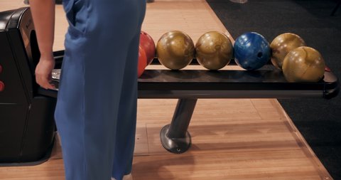 Unrecognizable person in blue trousers choose bowl for bowling game. Lower half. Coloured balls are in bowling machine. Close-up legs. Cropped shot