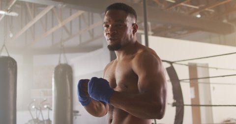 Video of fit african american man preparing for box training at gym. active, fit, sporty and healthy lifestyle, exercising at gym concept.
