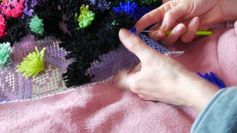 Hand embroidered carpet. A woman using a special hook and thread embroiders a carpet with blue threads. Handmade carpet embroidery. Women's hands create a pattern using multi-colored threads.