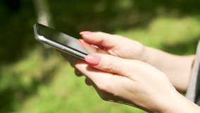 Girl Uses Mobile Phone, Watches Social Networks, Videos, Online Shopping. Girl's Finger Touches Center of Cell Phone, Hand Flips Slides over  Smartphone Screen in Nature, Close-up, Side View. 
