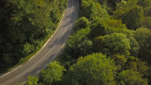 The car drives along mountain roads at sunset. A quadcopter shoots mountains. Flight of the camera over a mountain serpentine.