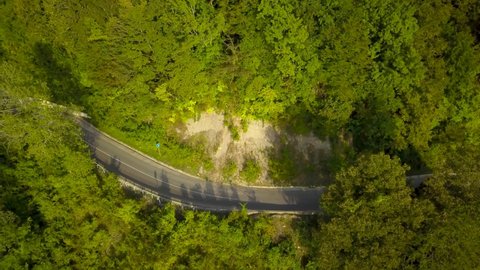 The car drives along mountain roads at sunset. A quadcopter shoots mountains. Flight of the camera over a mountain serpentine.