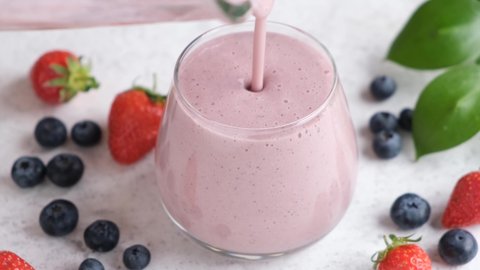 Pouring pink berry smoothie in glass. Healthy summer drink, berry milkshake or smoothie