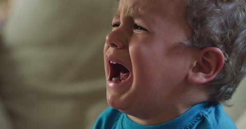 Cinematic authentic close up shot of sad upset little toddler boy is crying desperate with hurt face expression at home.