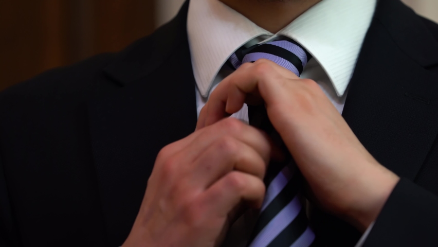 Man in suit tying a tie. Businessman in black suit tying the necktie. Face not visible. man getting dressed.  Man is preparing to go to work(office). Bloom before wedding ceremony.
