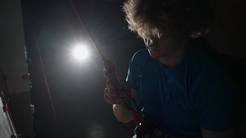 Young man professional climber training on a climbing wall, practicing rock-climbing and descends from the cliff using insurance, cinematic lighting.