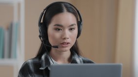 Asian female office worker wears headset has distant conference video calling with laptop computer. Korean businesswoman customer service manager client helpline agent online service speaking webcam