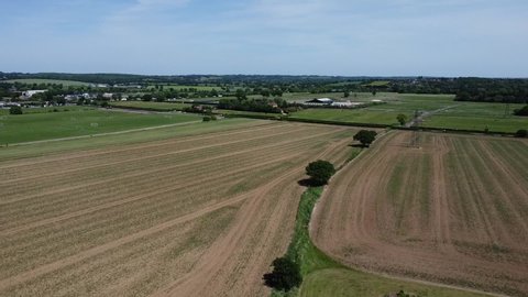 drone flying over a field in the english countryside during a summer day with road in background and moving cars