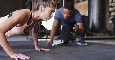 Video of african american male trainer motivating caucasian woman for doing push ups. active, fit, sporty and healthy lifestyle, exercising at gym concept.
