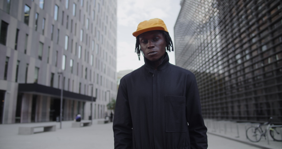 Young african american man standing near the office building and looking at camera. Thoughtful dark-skinned guy on the street 