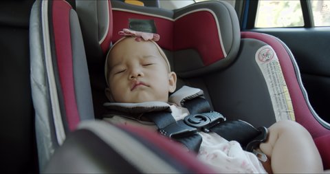 Cute Asian baby girl sleeping comfortably in car seat while vehicle driving. Toddler practice for safe car travel. Asia law enforcement for passenger safety product concept.