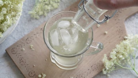 Pouring homemade elder flower syrup into a glass with ice