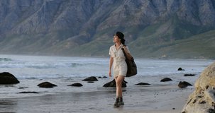 a thin girl traveler in mountain overalls and boots walks along the ocean beach, a strong wind blows. Inspiring wanderlust motivational shot of travel blogger or influencer walk on the Beach.