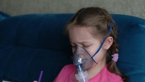 Little girl makes an inhalation vapor and draws a drawing. Child is sick and breathes through an inhaler in home. 