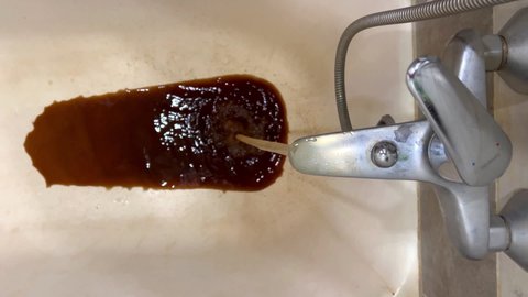 Vertical video from the bathroom. Disgusting dirty brown rusty water flows from the faucet after turning off the water. Annual shutdown of water in Russia.