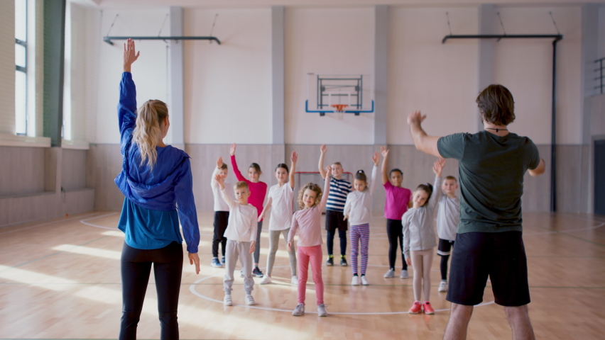 Rear view of PE teachers and group of elementary students exercising during class at school gym. Royalty-Free Stock Footage #1090418041