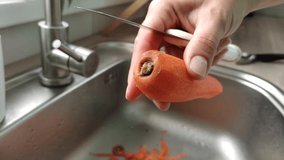 A woman is peeling carrots, hands close-up. The cook peels carrots to make soup or another dish. slow motion video.