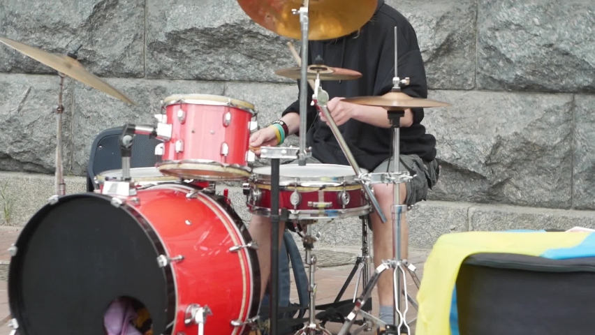 street musician hold drumsticks in hand, people vigorously beat them on cymbals during the daytime on the street, maybe it
