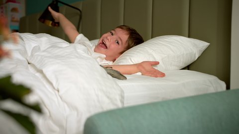 Six-year-old boy funny cheerful little child in white pajamas wakes up in bed in the morning. Face of a sleeping child baby on its side. Tracking shot sleeping baby at midnight. Sleeping baby in bed.