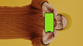 look at the phone - young man showing mobile phone blank screen orange background studio shot medium shot vertical video. High quality 4k footage