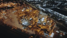 Drone footage of urban landscape, covered in a thick smog over industrial area at night. Huge manufacturing site at city suburbs, lit by the bright lighting as seen from above. High quality 4k footage