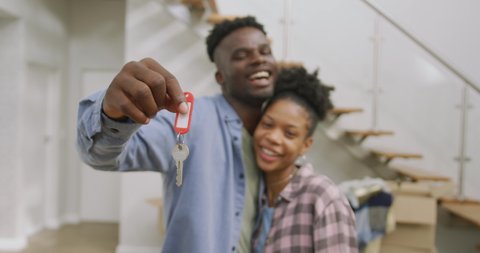 Video of happy african american couple embracing, showing keys to new house. love, relationship, and starting new life together.