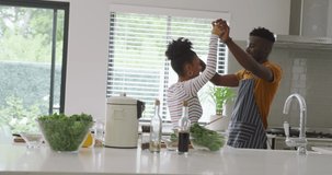 Video of happy african american couple dancing while cooking together in kitchen. love, relationship, togetherness and spending quality time at home.
