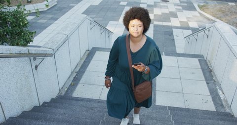Plus size biracial woman walking on stairs with smartphone in city. digital nomad on the go, body inclusivity.