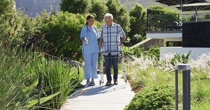 Video of happy biracial female doctor taking care of caucasian senior man in rest home garden. seniors health and nursing home lifestyle concept.