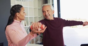 Video of happy biracial female physiotherapist exercising with caucasian senior man. seniors health and nursing home lifestyle concept digitally generated video.