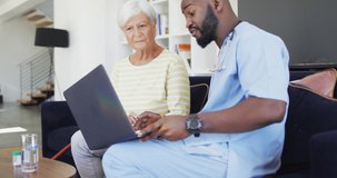 Video of african american male doctor using laptop with caucasian senior woman. seniors health and nursing home lifestyle concept.