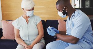 Video of african american male doctor in face mask vaccinating caucasian senior woman. seniors health and nursing home lifestyle concept.