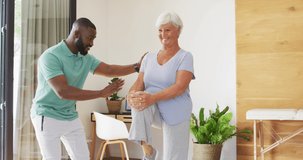 Video of happy african american male physiotherapist exercising with caucasian senior woman. seniors health and nursing home lifestyle concept.
