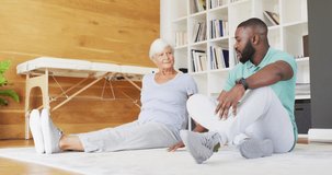 Video of african american male physiotherapist exercising with caucasian senior woman. seniors health and nursing home lifestyle concept.