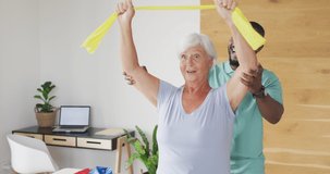 Video of happy caucasian senior woman exercising with african american male physiotherapist. seniors health and nursing home lifestyle concept digitally generated video.