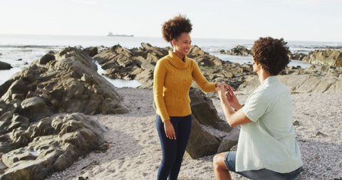 African american man putting a ring on his girlfriend's finger on the rocks near the sea. love and relationship concept