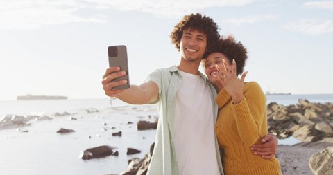 African american couple taking a selfie and showing their ring standing on the rocks near the sea. love and relationship concept