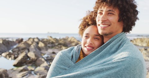 African american couple wrapped in blanket standing on the rocks near the sea. love and relationship concept