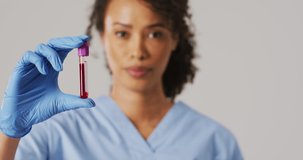 Video of biracial female doctor holding test tube on blue background. global medicine and healthcare concept.