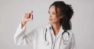 Video of biracial female doctor holding test tube on white background. global medicine and healthcare concept.