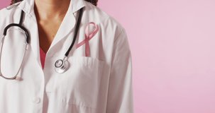 Video of biracial female doctor with pink breast cancer ribbon. global medicine and healthcare concept.